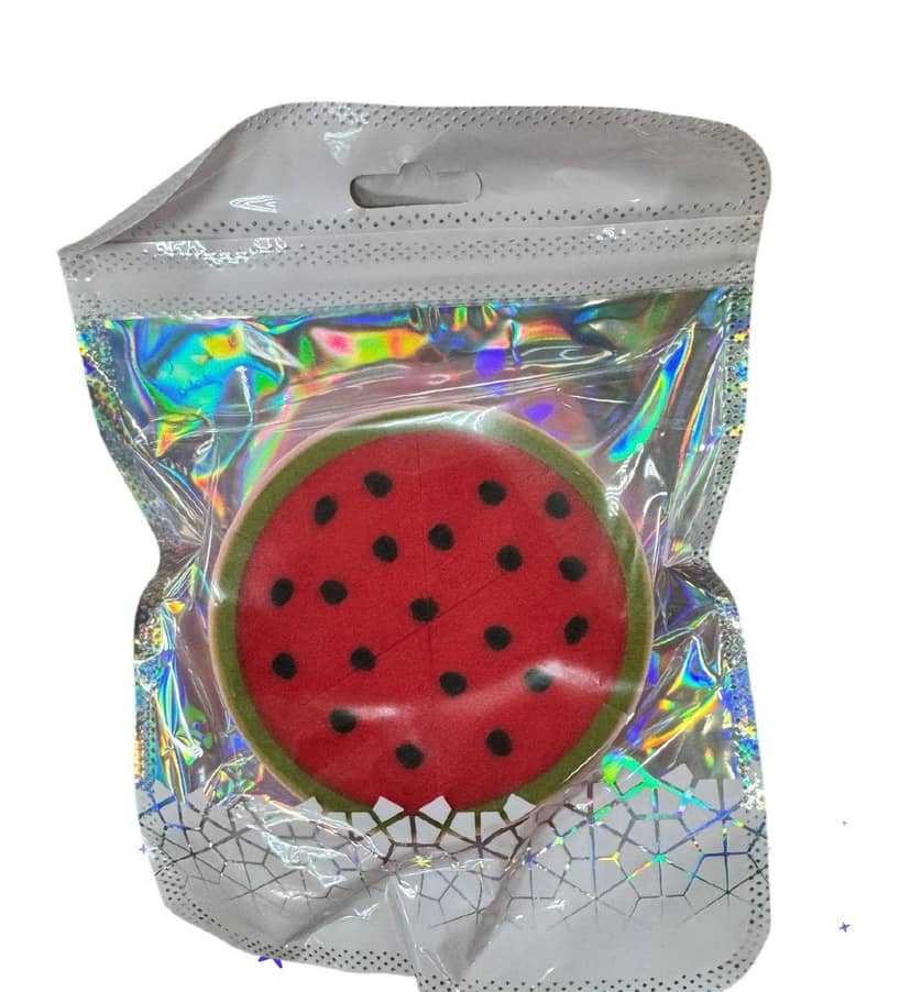 Round red sponge with black dots imitating watermelon seeds, framed with green trim, packaged in